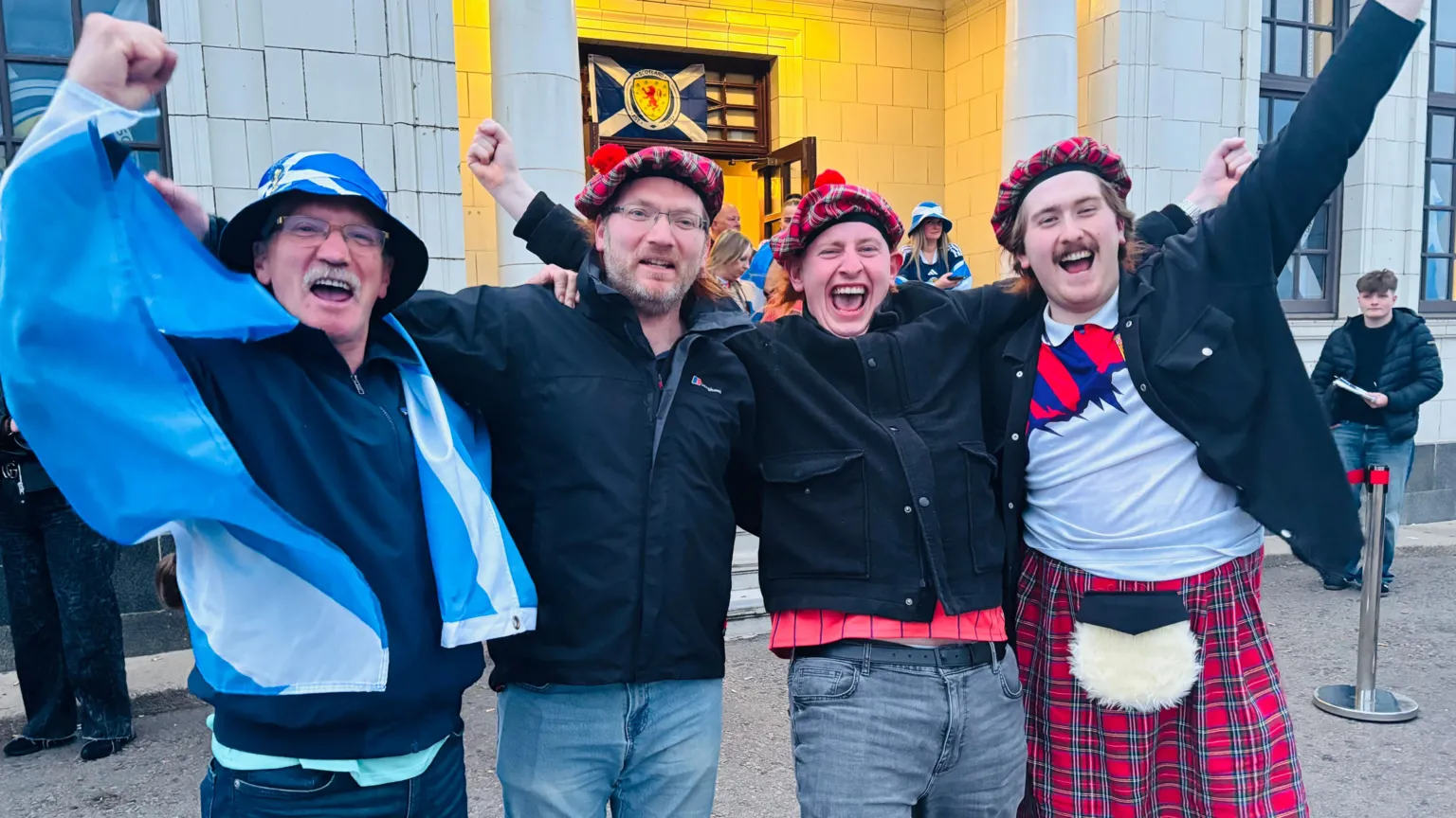 Standing outside the Beach Ballroom are (from left) Jim Stewart, 73, David Stewart, 49, Craig Stewart, 31, and 19-year-old Alex Stewart. They are cheering with their arms raised. Jim is wearing a saltire round his shoulders.