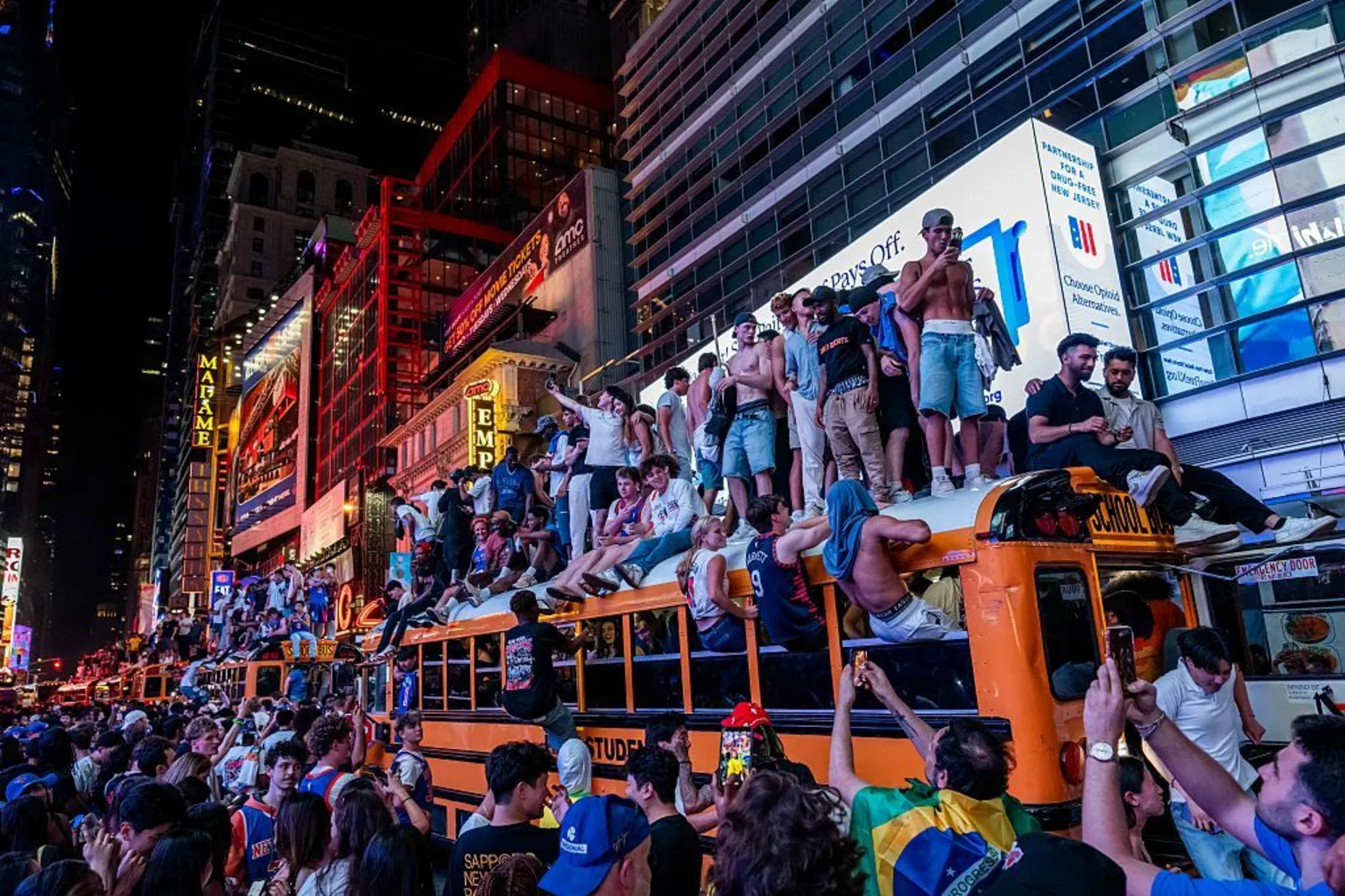 Dozens of people stand on top of a school bus parked in Manhattan, as others climb onto the vehicle.