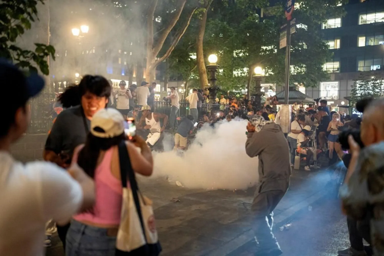 People run away in different directions from what appears to be a flare or firework that's produced a cloud of smoke in Manhattan, New York City at night time.