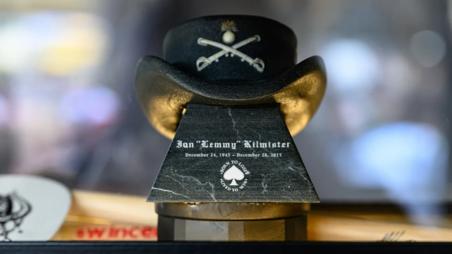 An urn with a cowbot hat perched on top opf it. The hat displays a logo of two crossed swords, and the urn, which is black, displays the words Ian 'Lemmy' Kilmister and the dated December 24 1945 to December 28 2015