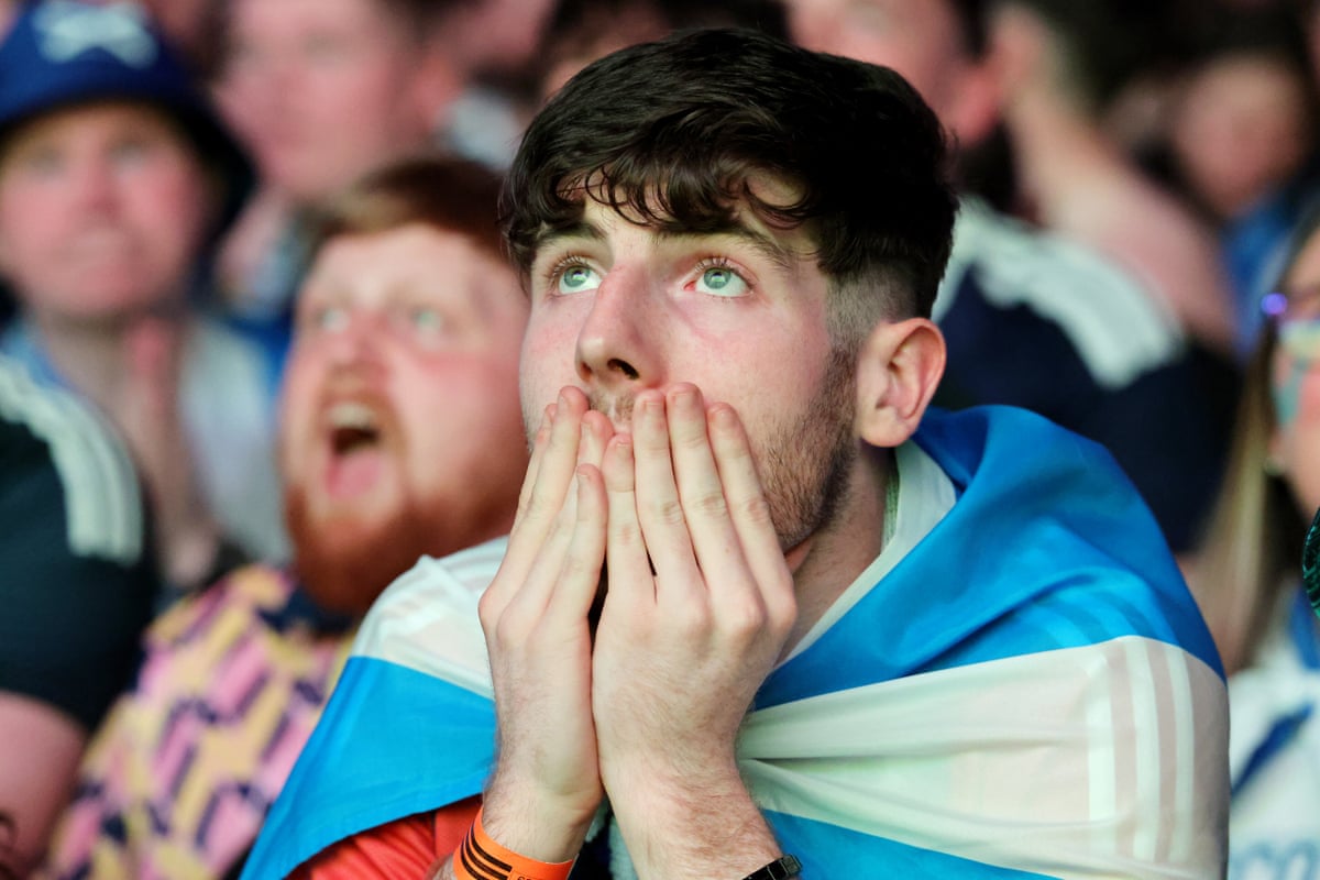 Close-up of fan with Scotland flag tied around his shoulders, holding his hands up to his mouth