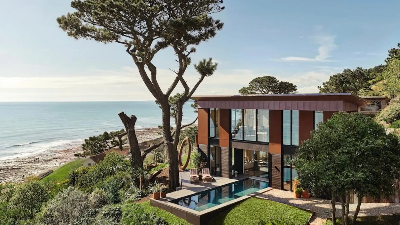 Omaze A large house by a beach in Cornwall. There are floor to ceiling windows, both upstairs and down. There is a pool at the front of the property