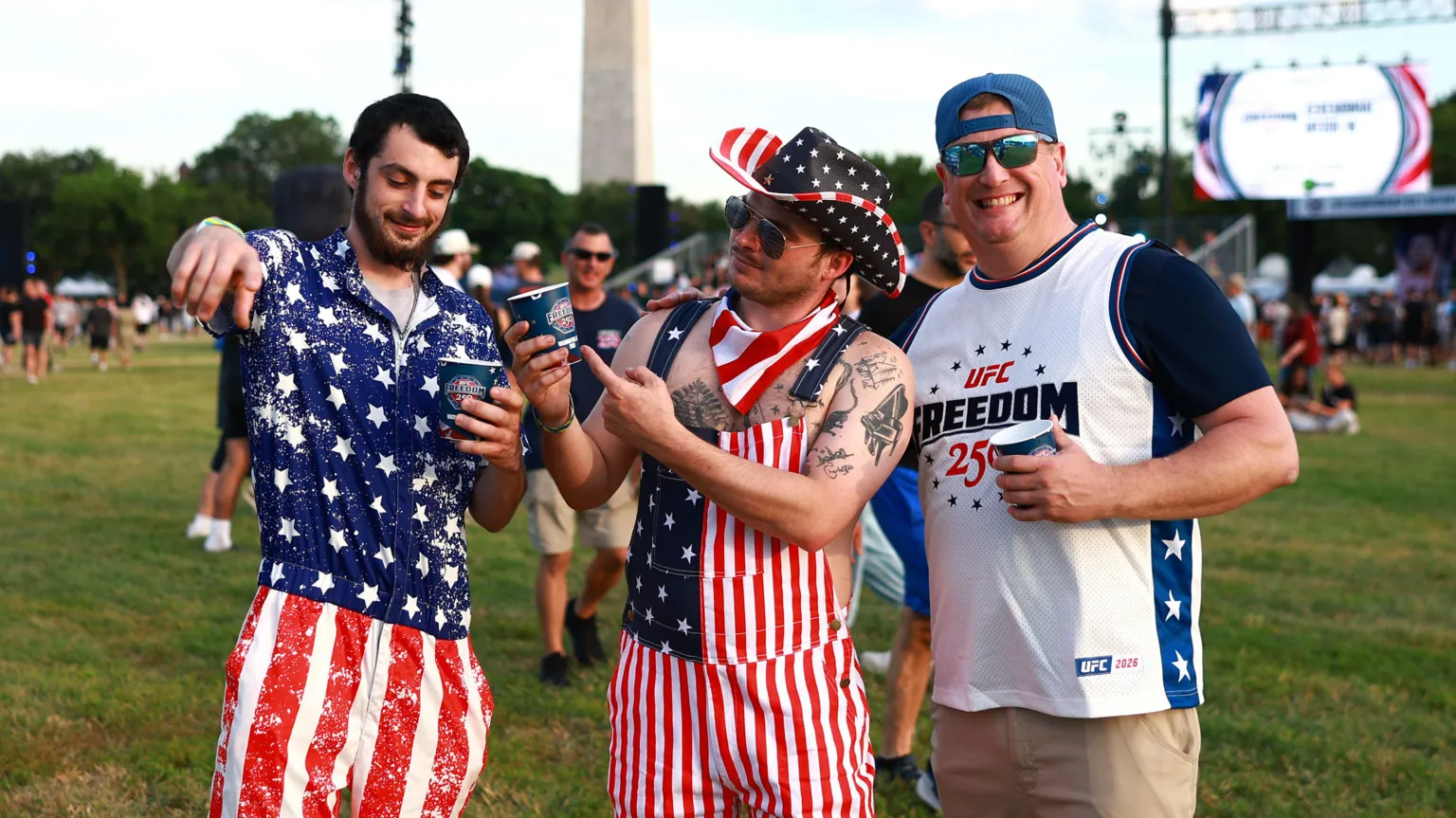 Three men pose for the camera - the two on the left are dressed in stars and stripes, while the man on the right smiles in a UFC Freedom 250 T-shirt