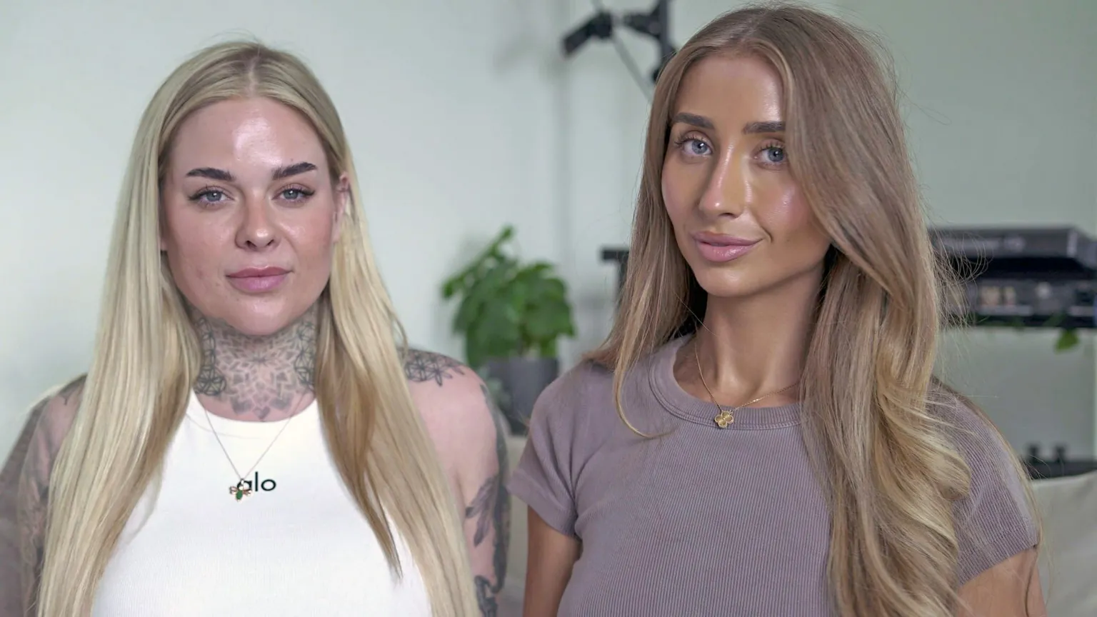 A head and shoulders portrait of OnlyFans creators Gia Clarke, on the left and Lily Phillips, on the right. They are looking into the camera smiling with their mouths closed. Gia wears a white tank top and has tattoos on her neck and shoulders, framed by long blonde hair. Lily has wavy light brown hair and a dark tshirt on. 