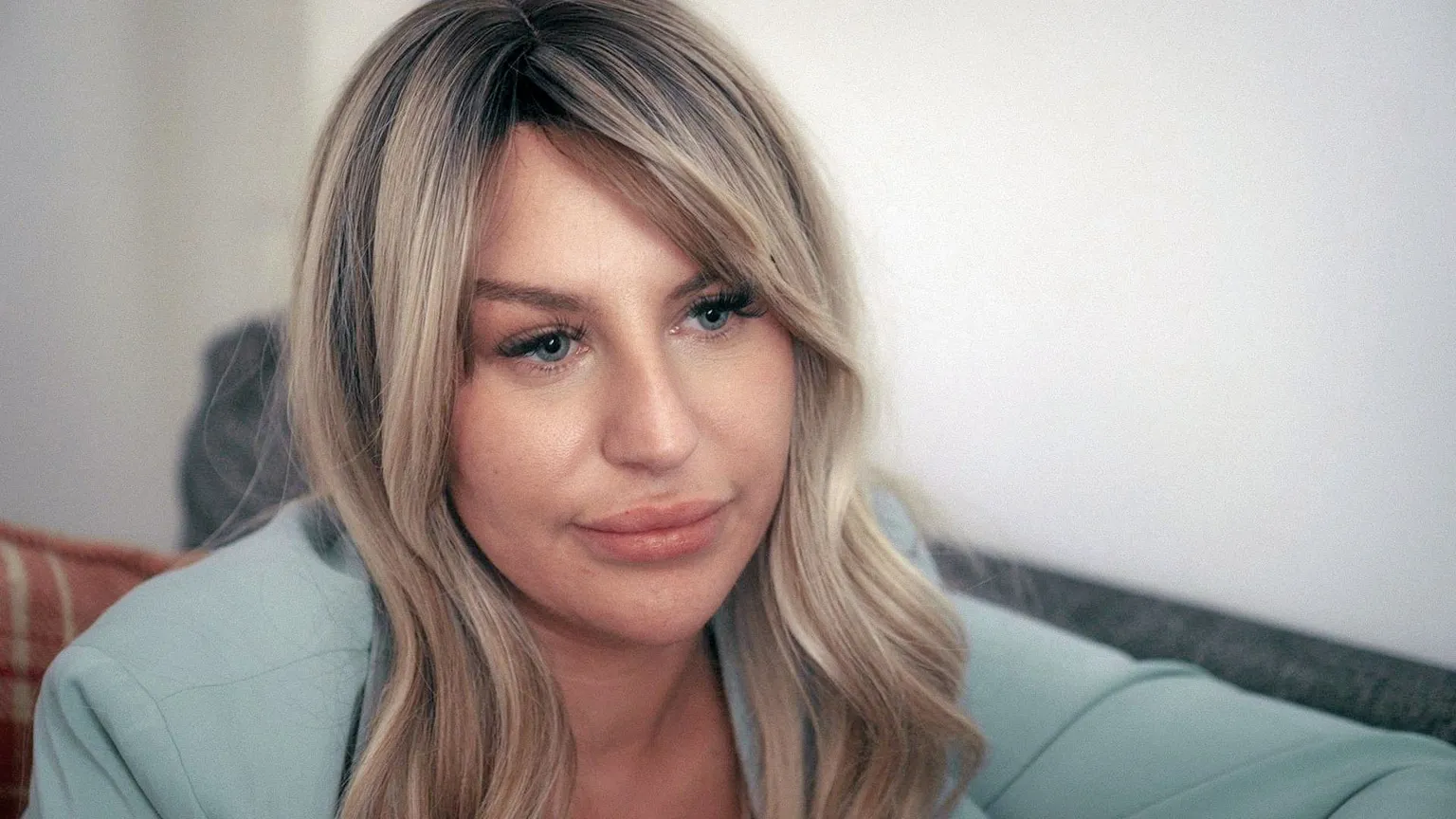 A portrait shot of Rebecca, looking sideways at someone behind the camera. She looks serious and her face is framed by wavy blonde hair. 