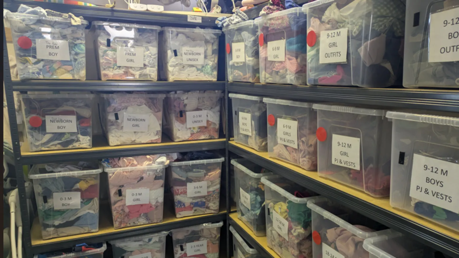 Emilie de Bruijn A small office space is full from ceiling to floor with boxes of different children's clothes. Signs on the front of the boxes identify who they are for
