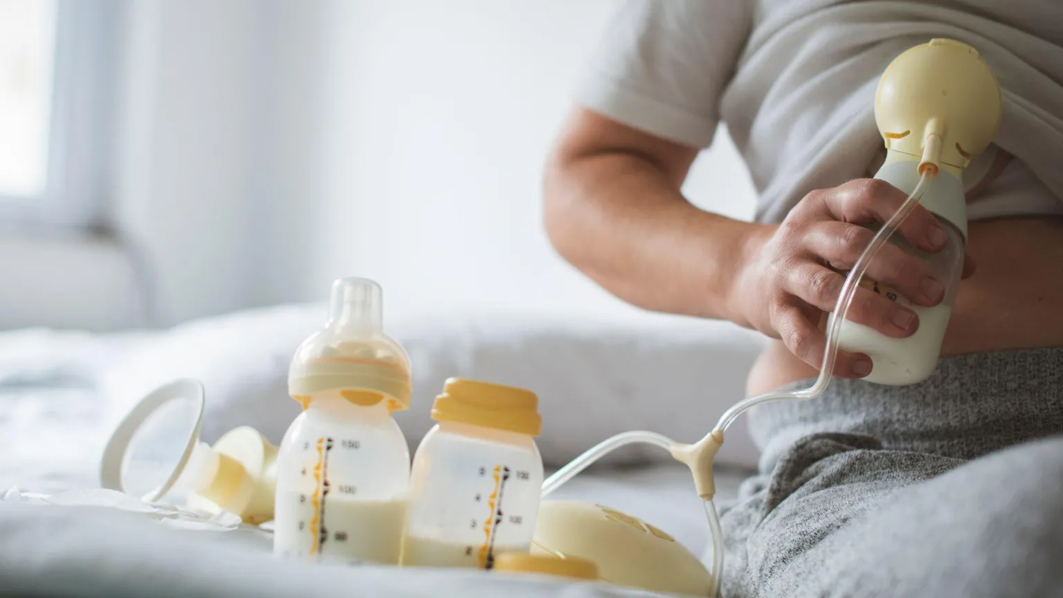  A woman uses a breast pump to express milk, with bottles of milk on the bed beside her
