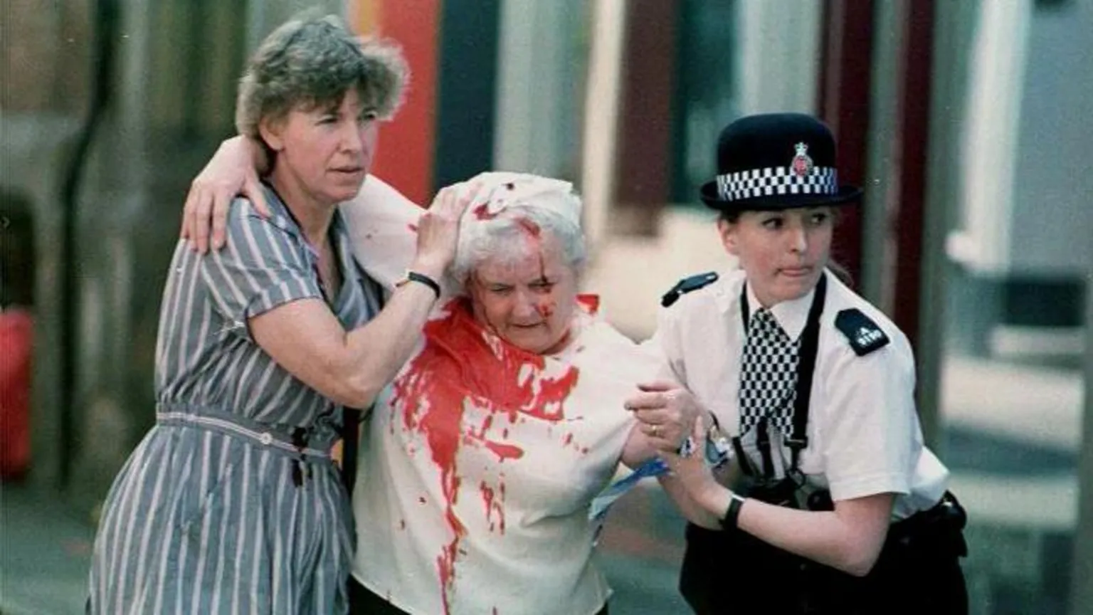 A female police officer and an unidentified woman help a woman wearing a blood-stained shirt in the aftermath of the IRA Manchester bomb in June 1996.