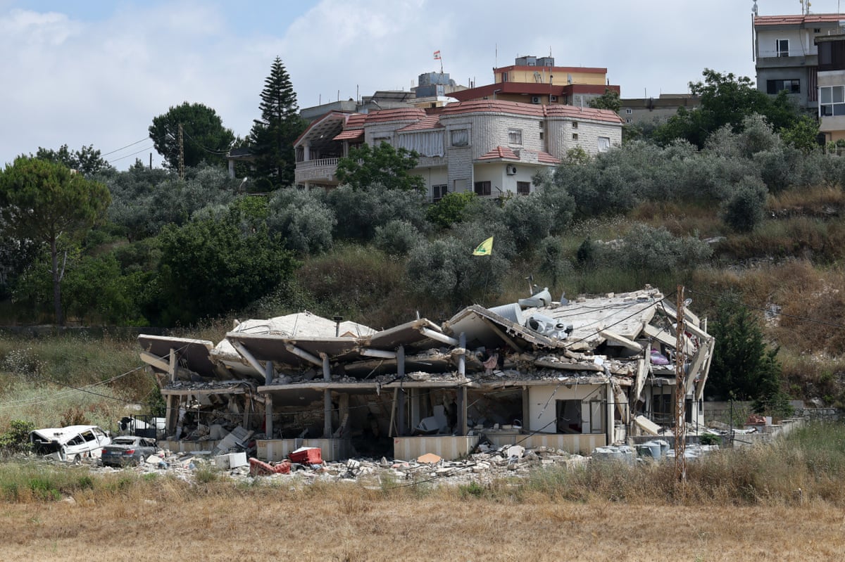 A destroyed building in a green space at the edge of a village.