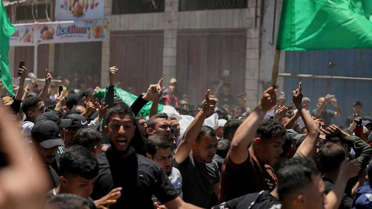 AFP via Palestinians carry the bodies of Imad Salim, also known as Abu Hassan, a senior commander in Hamas' armed wing, and others during a funeral procession in Gaza City last month. Men in black are pointing to the sky while some are waving green flags.