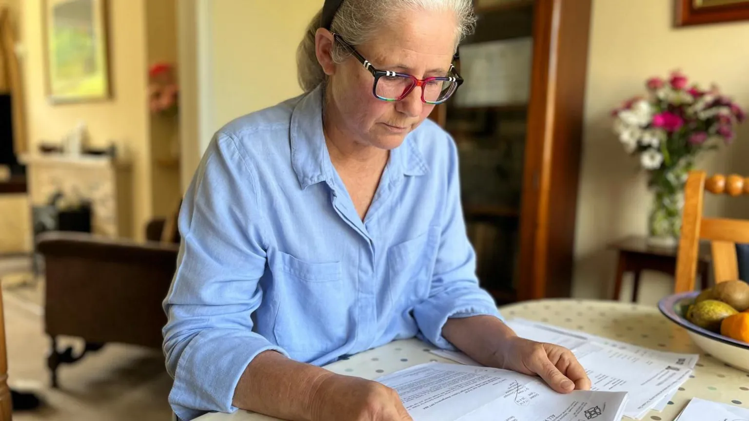 Heather is sat at her dining table, looking at the letters she kept when she wrote to the all-Wales genetic service asking for testing in 2014.