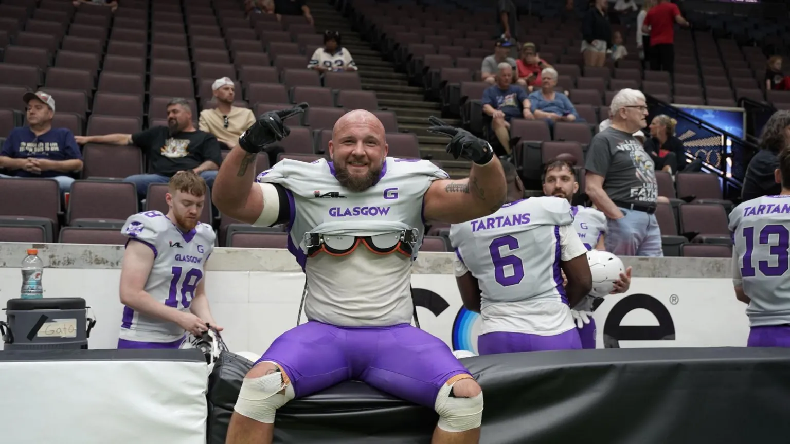 Declan Clay An American Football player, sitting on a barrier in front of fans, wearing a white and purple uniform