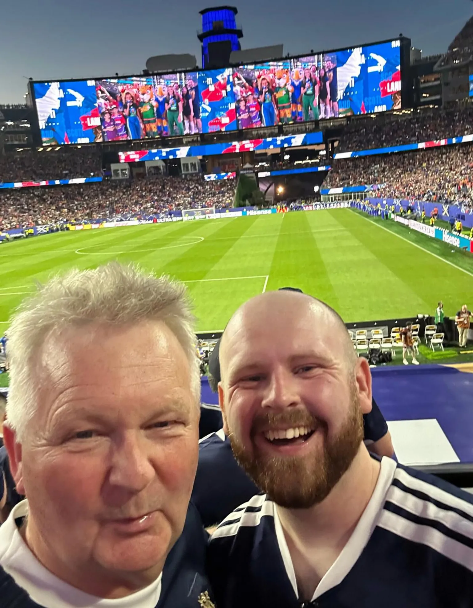 Peter Aitchison Two men in a selfie with a football pitch and big screen behind them
