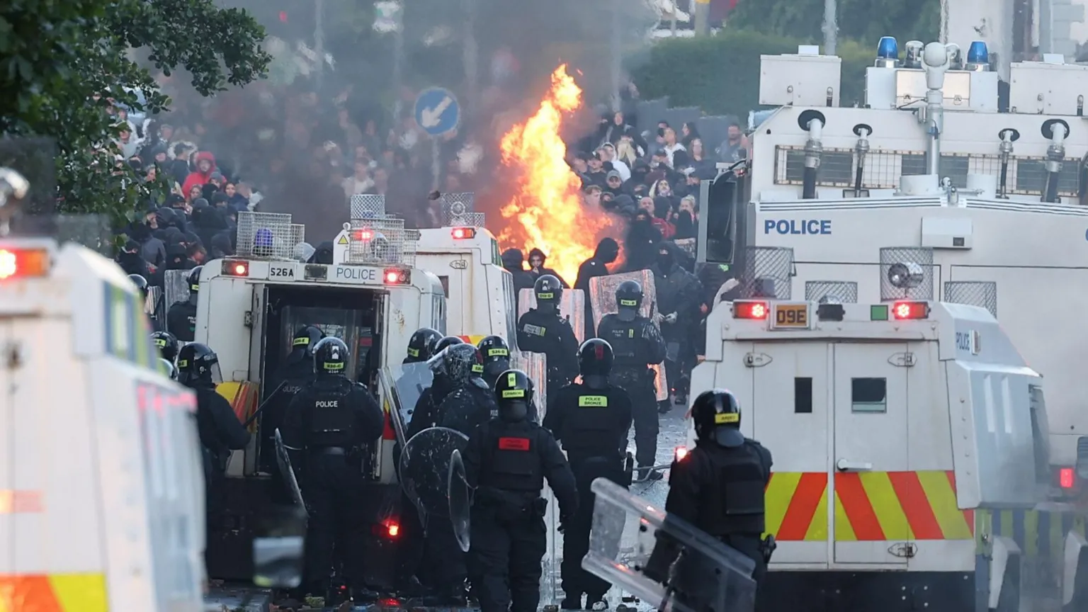 EPA Flames are visible in the middle of the road between police officers in riot gear and land rovers and a large crowd