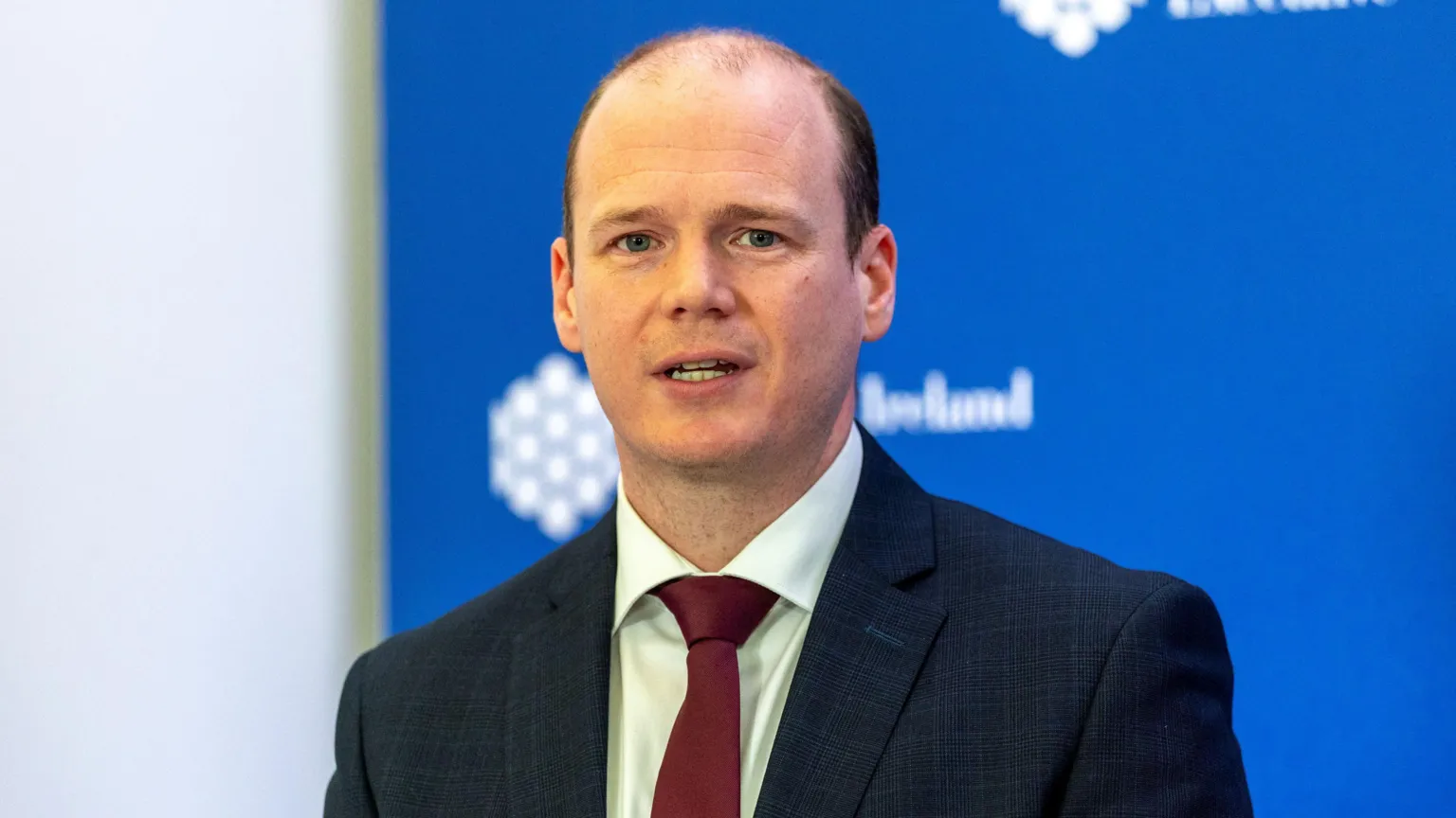 Gordon speaking. He is wearing a navy suit, burgundy tie and a white shirt.