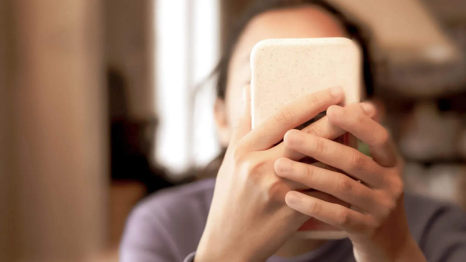  A young girl hold a smartphone in front of her face. Her face cannot be seen.