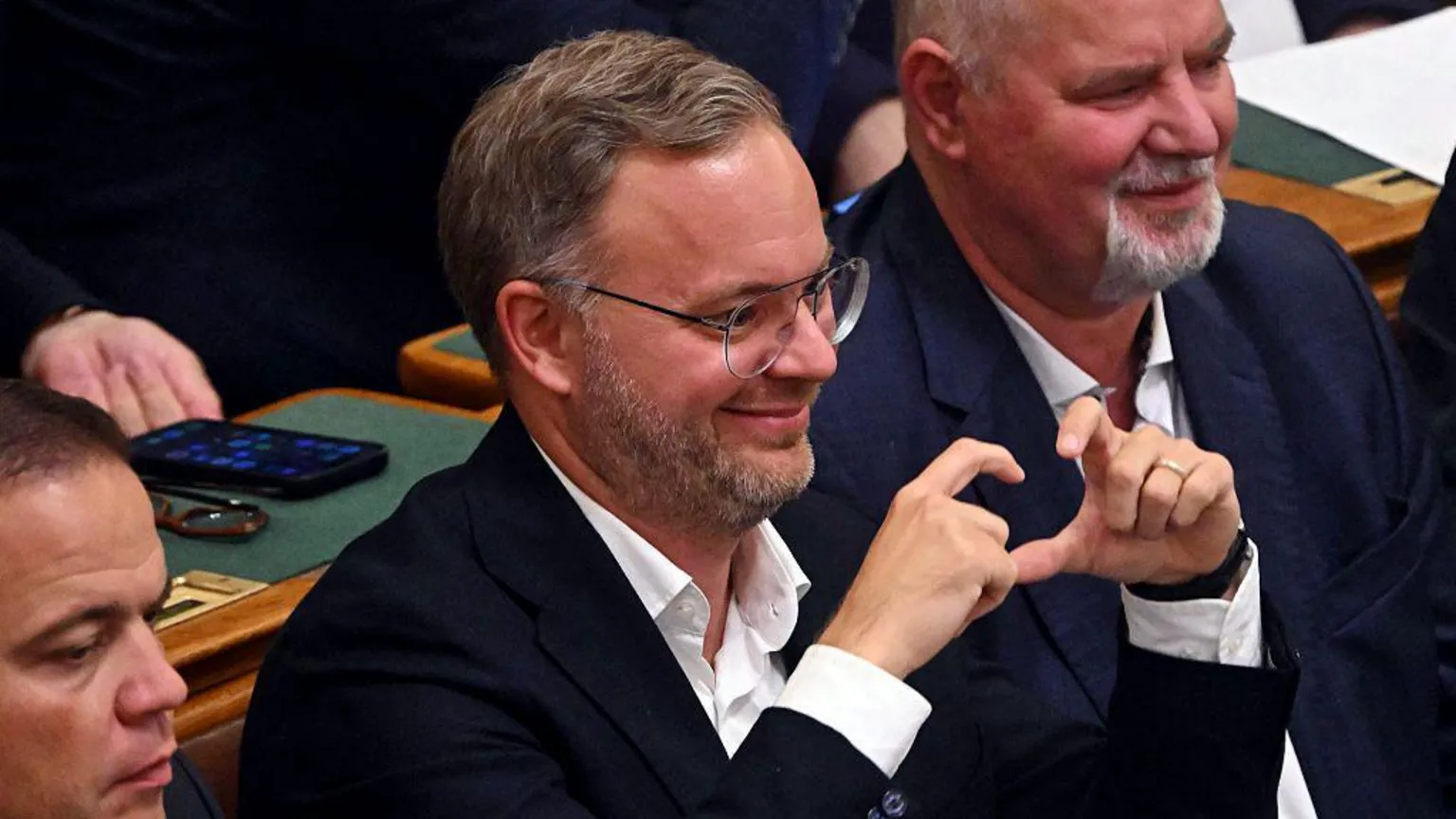 AFP via Balázs Orbán makes a sign with his fingers as he grins in parliament