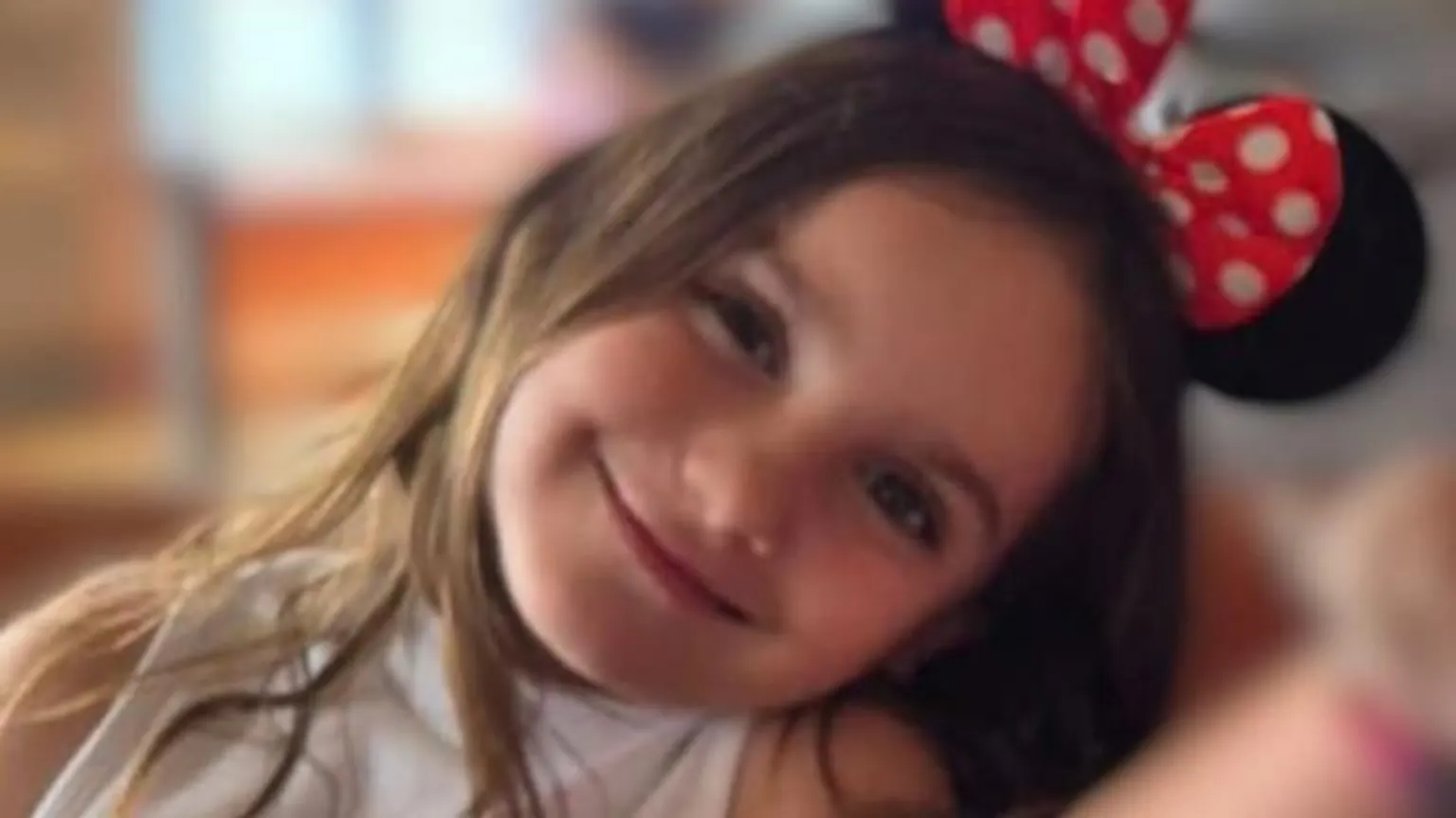 Family handout Aria Thorpe. She has long dark hair and is wearing Minnie Mouse ears. Her head is tilted and she is looking at the camera and smiling.