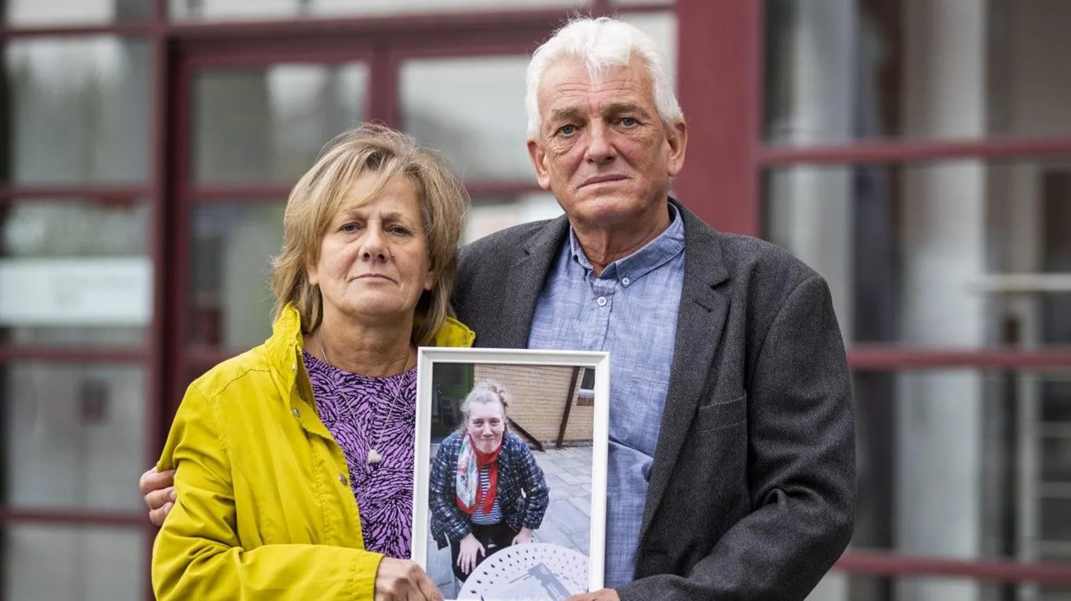 A man and a woman standing beside each other. They are holding a framed photo of a woman.