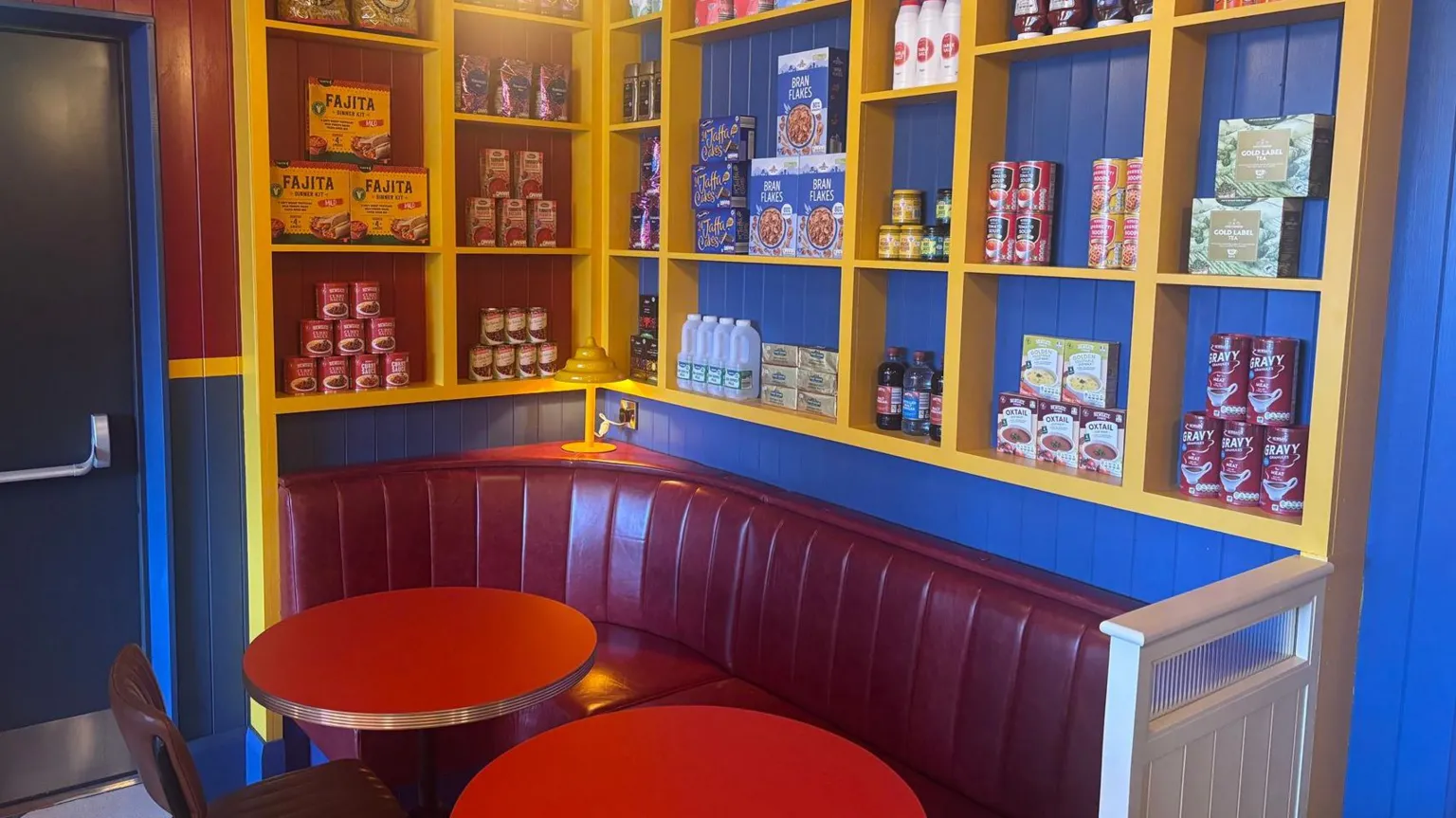A booth in the bar with two rounds red tables and blue walls with a grocery display on the wall