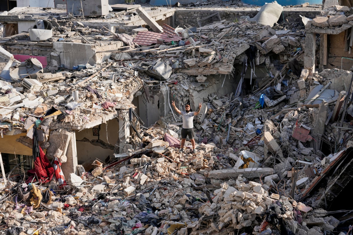 A man displays peace signs with his hands as he stands on the rubble of his destroyed house.