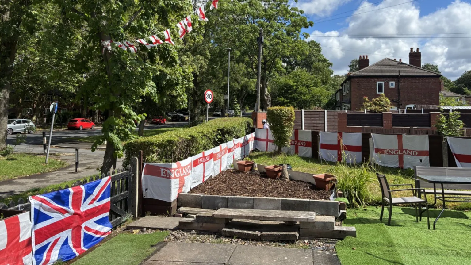 A garden with England flags all over the fences and bunting connected to a nearby tree.