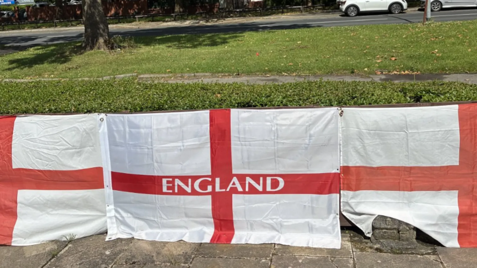 A line of England flags attached to a garden fence in front of a road