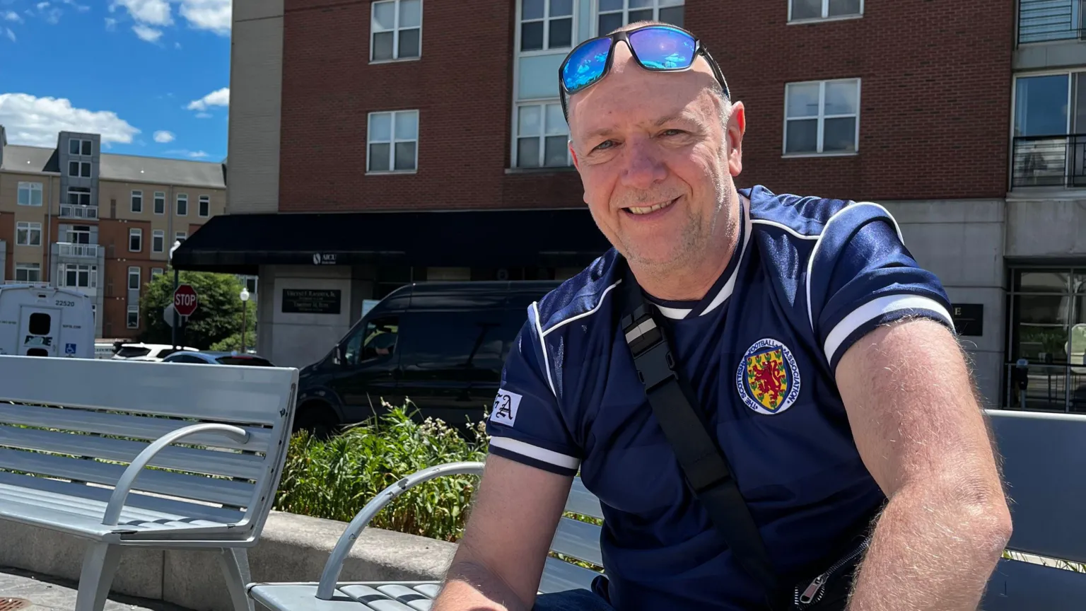 A man wearing a Scotland top with blue sunglasses on his head 