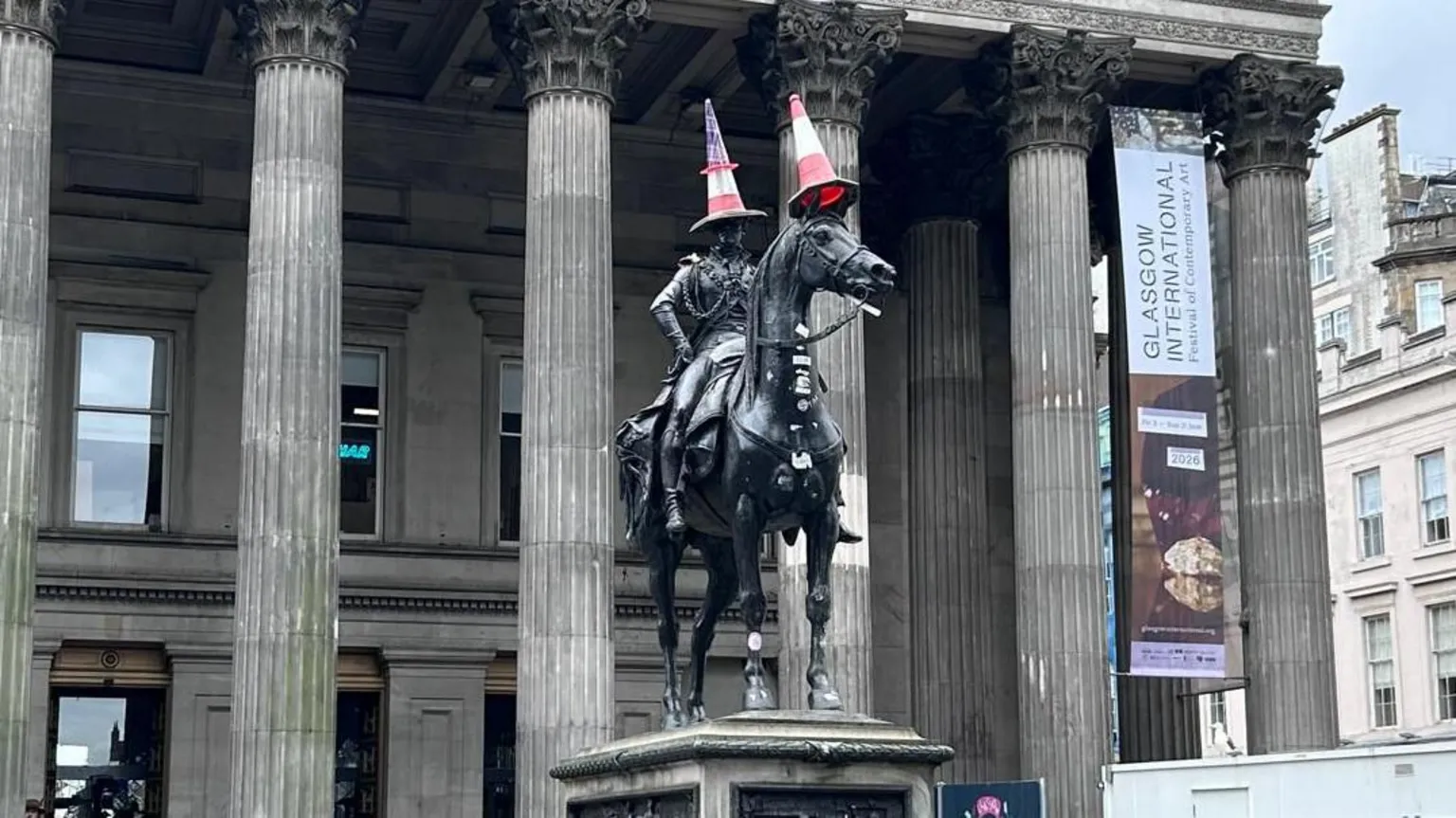 Duke of Wellington statue in Glasgow. It is a man sitting on a horse. There are orange traffic cones on the man's head and the horse's head.