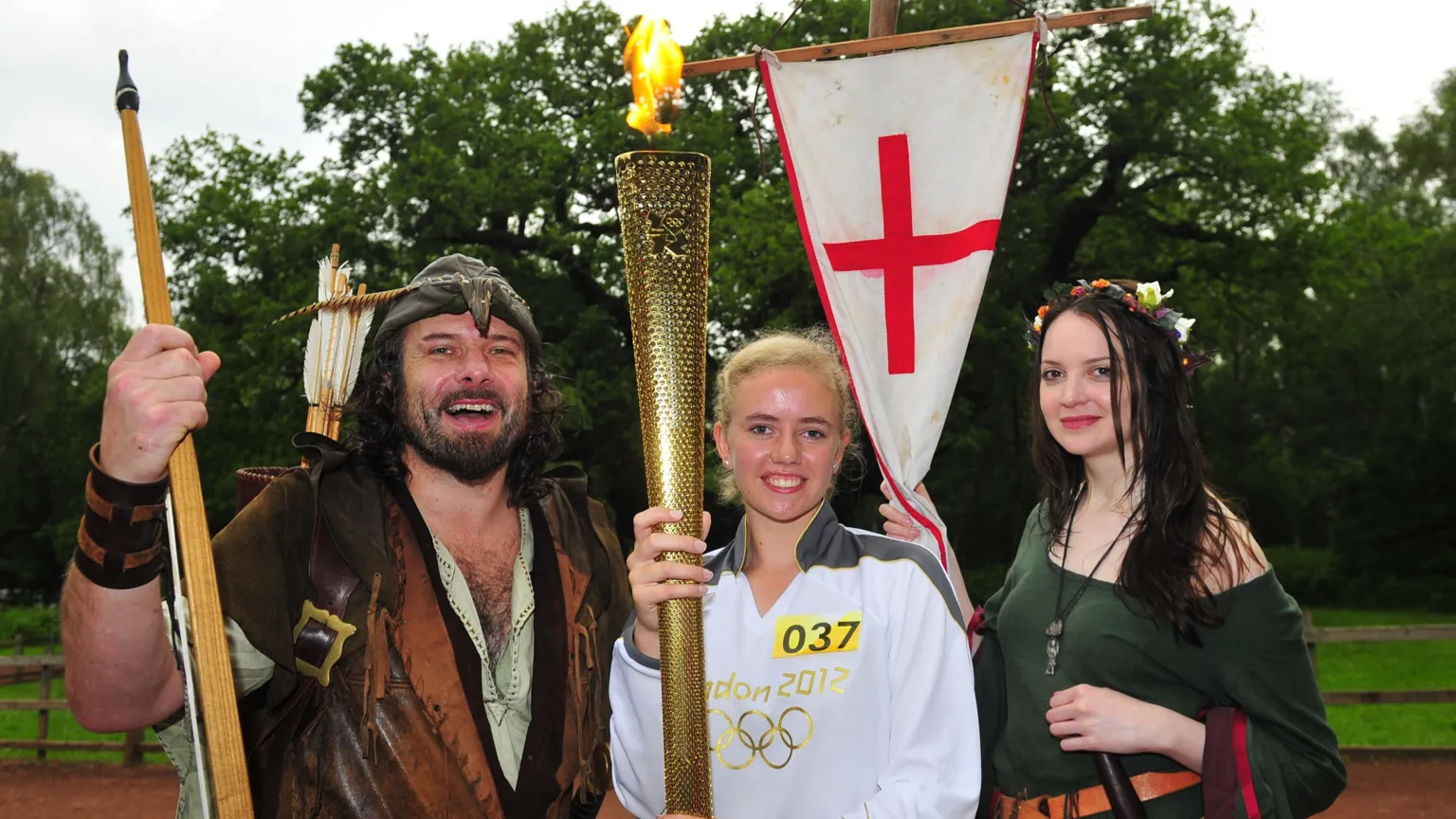 LOCOG via JUNE 28: In this handout image provided by LOCOG, Torchbearer 037 Laura Graves stands in front of The Major Oak in Sherwood Forest whilst holding the Olympic Flame alongside 21st century Robin Hood Ade Andrews and Sylvia Robson on Day 41 of the Olympic Flame Torch Relay leg on June 28, 2012 in Nottingham, England. The Olympic Flame is now on day 41 of a 70-day relay involving 8,000 torchbearers covering 8,000 mile