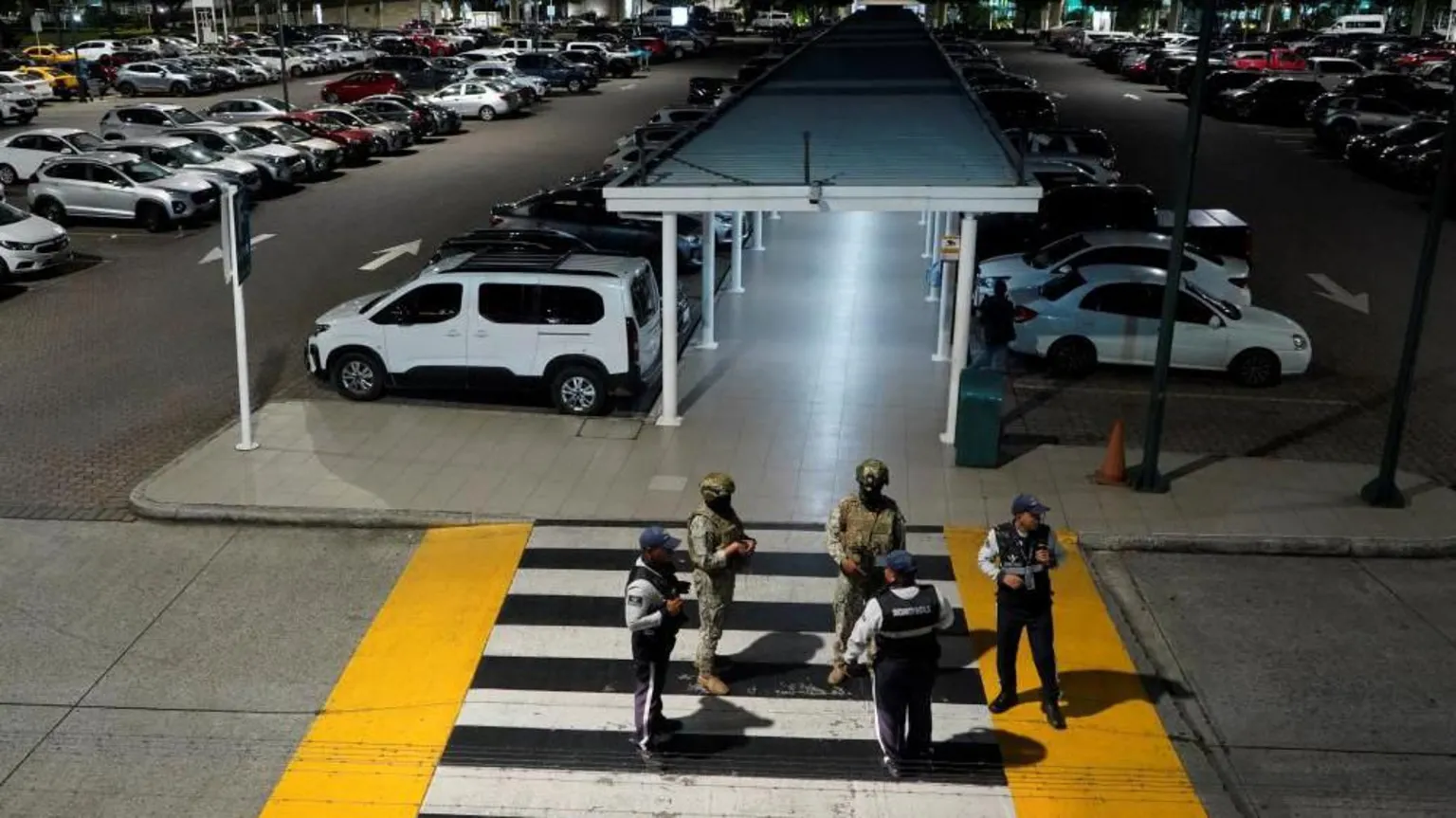 /Cesar Munoz Members of Ecuador's armed forces stand stand guard after an armed attack at the airport in Guayaquil. There are two soldiers with guns and three other uniformed men standing on a pedestrian crossing leading to the parking lot. 