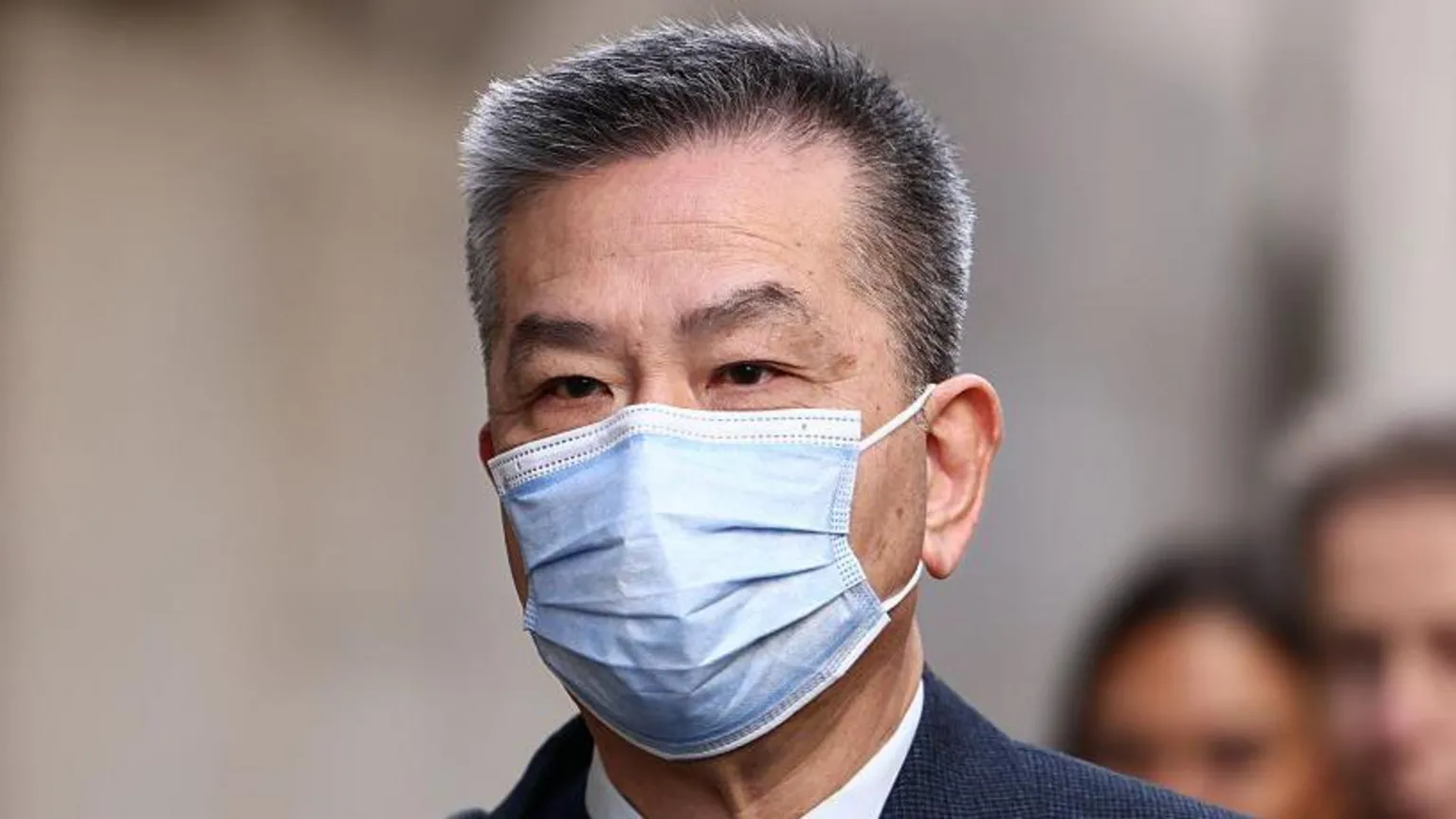 A shot of Chung Biu Yuen, a man wearing a surgical face mask, from the neck up. His hair is black with grey tips and he is wearing a suit