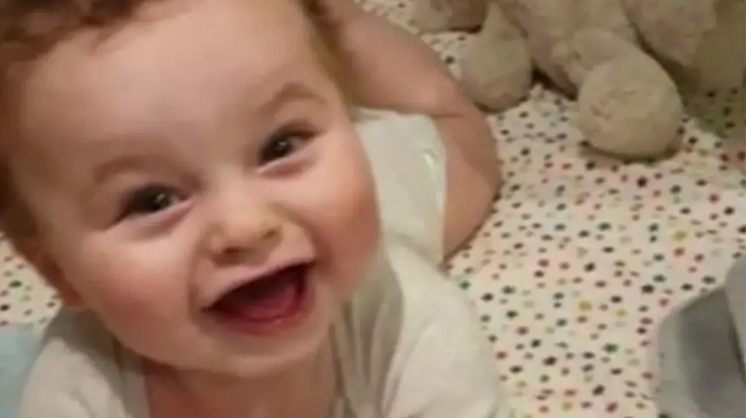 Lancashire Police Baby Preston Davey smiles at the camera dressed in a white vest. He appears to be lying in a cot with a star-covered bedsheet.