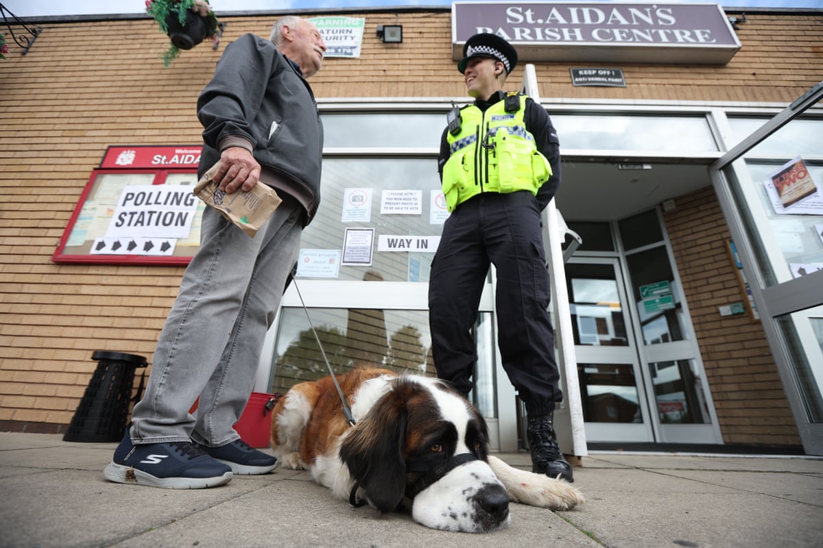 A voter speaks to a police officer as Saint Bernard dog called Indie waits at a polling station in Wigan, Britain, 18 June 2026.