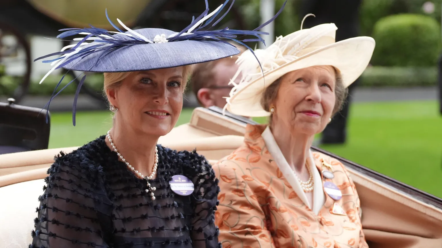 Sophie, the Duchess of Edinburgh and Anne, the Princess Royal, wearing blue and white hats respectively and wearing a blue dress and orange dress respectively.