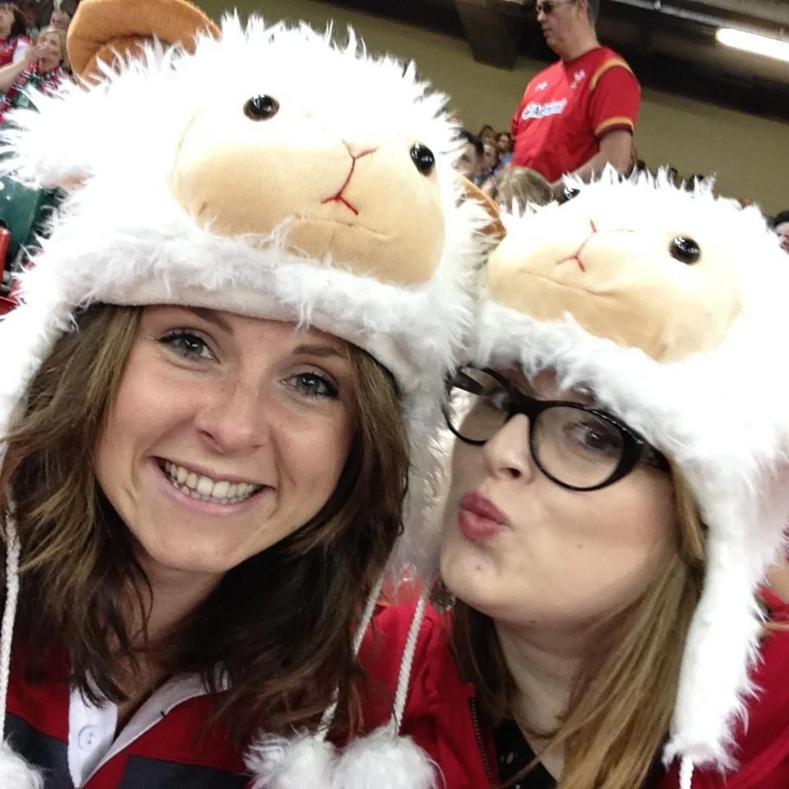 Gemma Hicks Gemma and Helen taking a selfie in the stand of the Principality Stadium. Gemma has shoulder-length wavy dark hair While Helen has blonde hair and is wearing bold, dark-framed glasses. Both are wearing sheep hats and Gemma is smiling while Helen is pouting