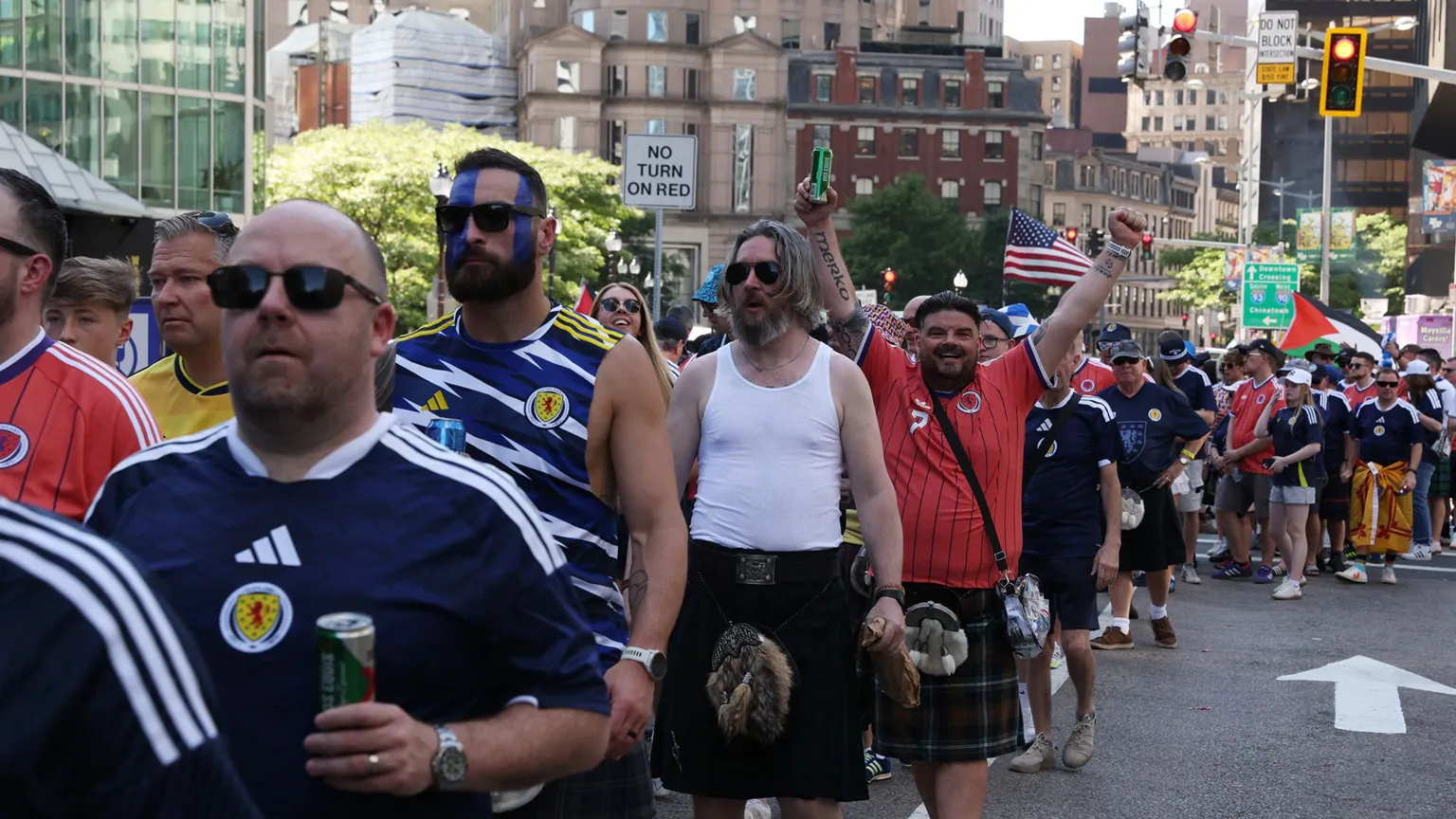 Men in blue or red Scotland strip, many in kilts, queue on an American street