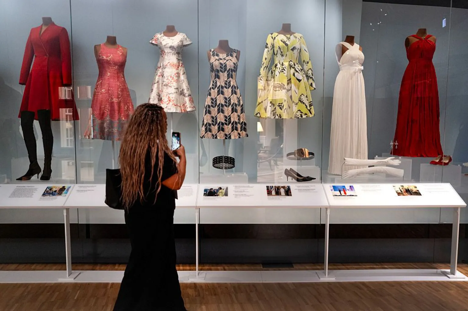 Scott Olson/ A woman views a selection of dresses worn by Michelle Obama while she was first lady. The dresses are patterned and displayed on mannequins, accompanied by the shoes and other accessories worn with them.