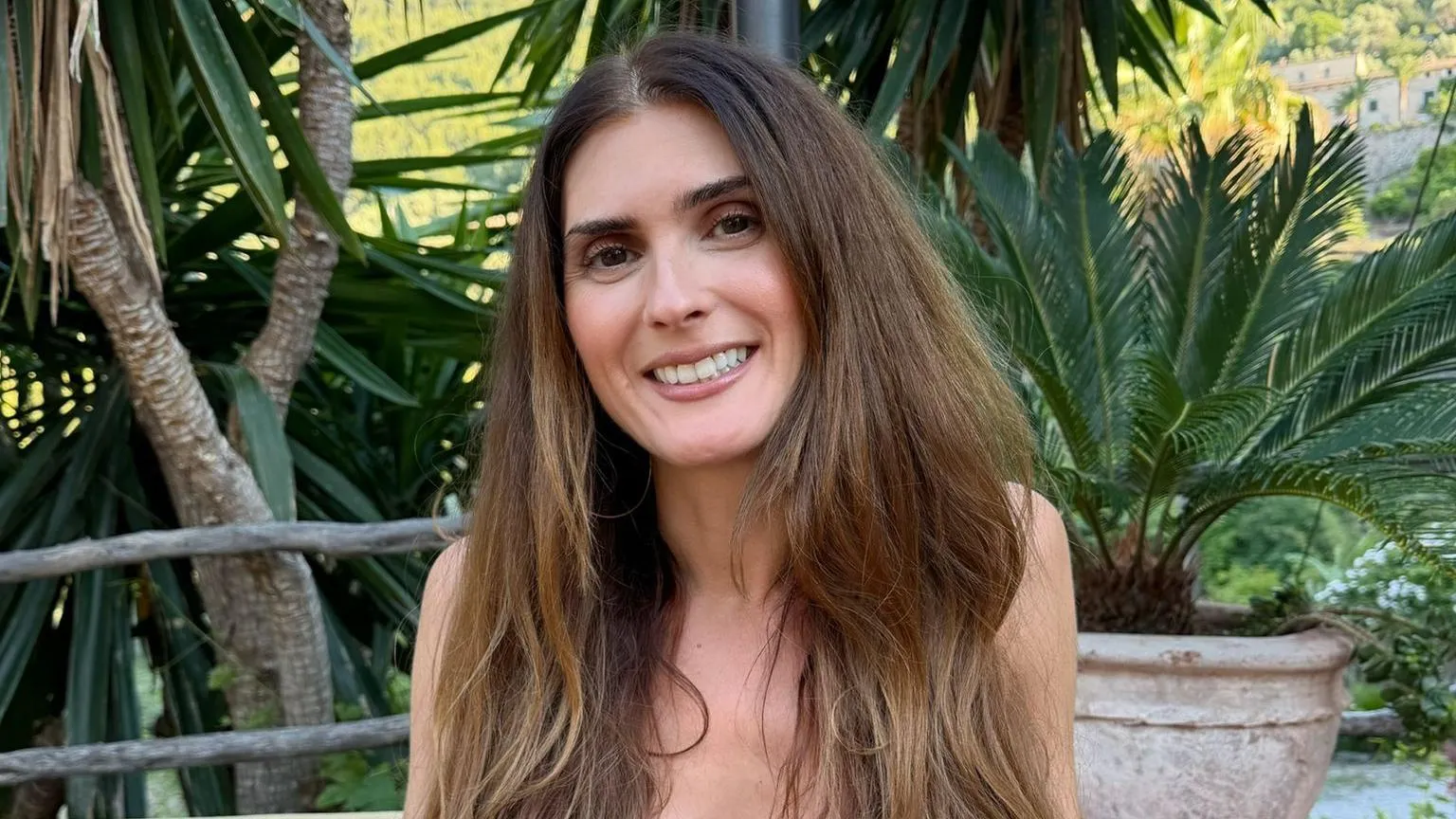 Yasmin El-Saie Woman with long brown hair smiling at camera with plants behind her