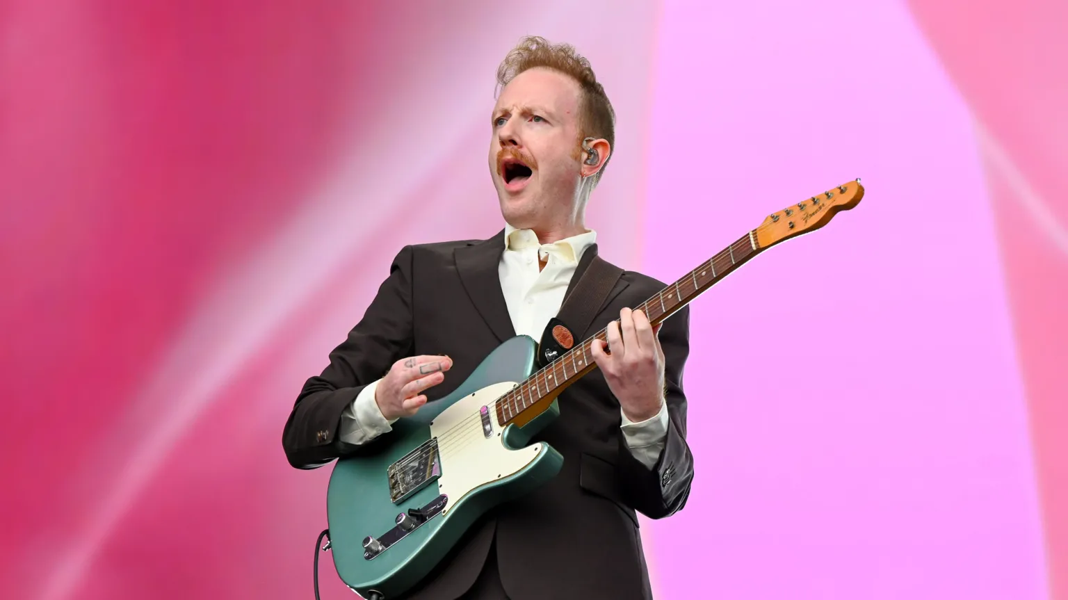 Two Door Cinema Club performing at Reading Festival, with singer/guitarist Alex Trimble shouting out. He is dressed in a suit and holding a guitar.
