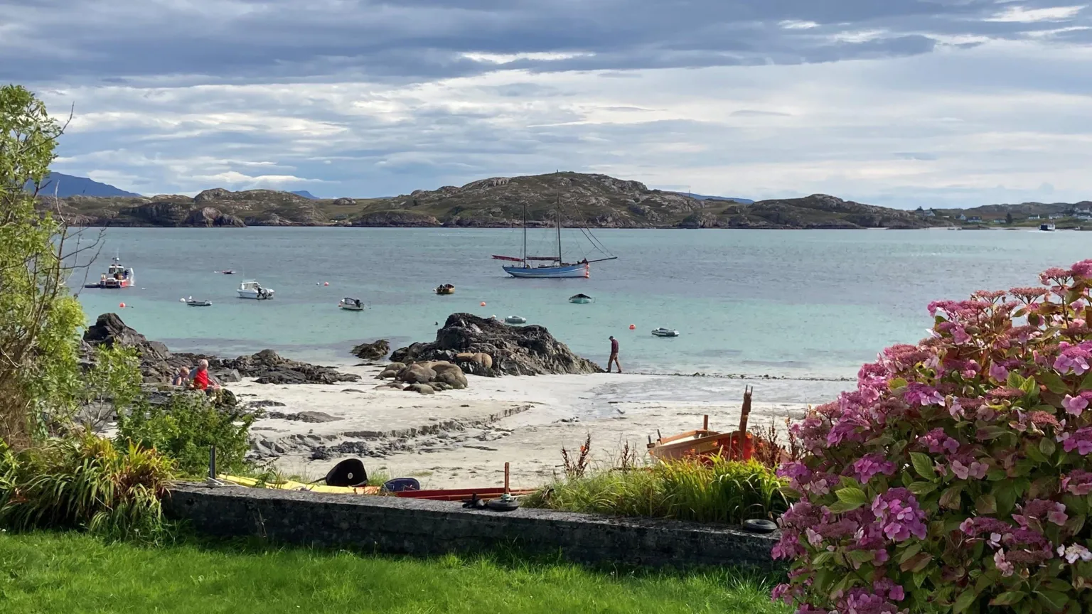 Ian Thornton A view from a garden onto beach and then water, with a sailing boat in view, and then more land in the distance.