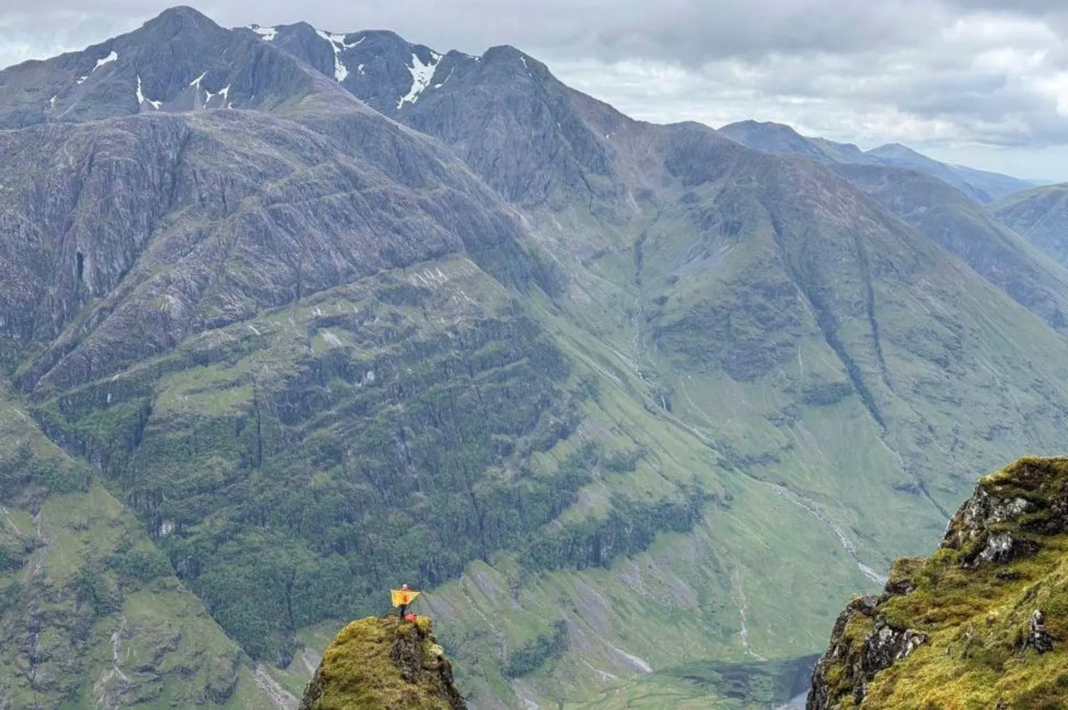 Cumming Finlay A man standing on a high ridge holding a Lion Rampant flag, with mountainside in the distance.