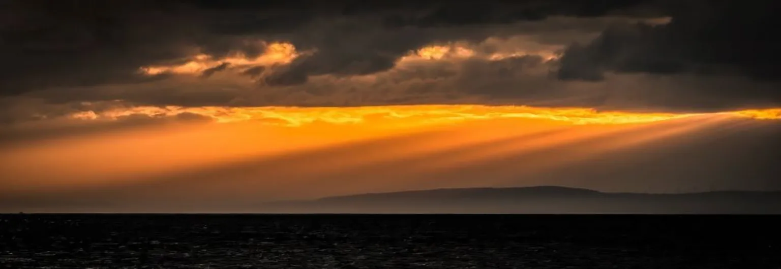 Craig Bradshaw An orange sunset glow over dark sea and hills.