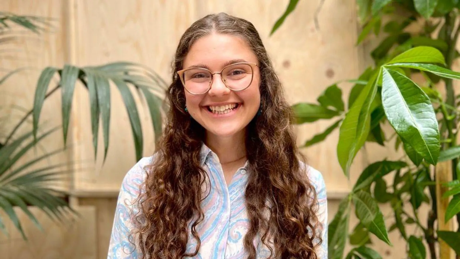 Jenny Kendall Jenny Kendall smiles at the camera, standing indoors in a room with lots of green plants. She has long curly hair and wears glasses, and a pale paisley shirt.