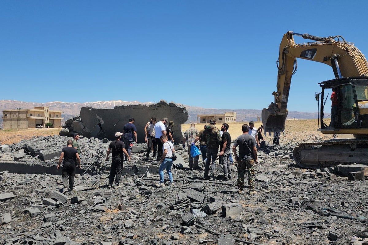 Over a dozen men stand stood near heavy machinery at the site of a bombing.