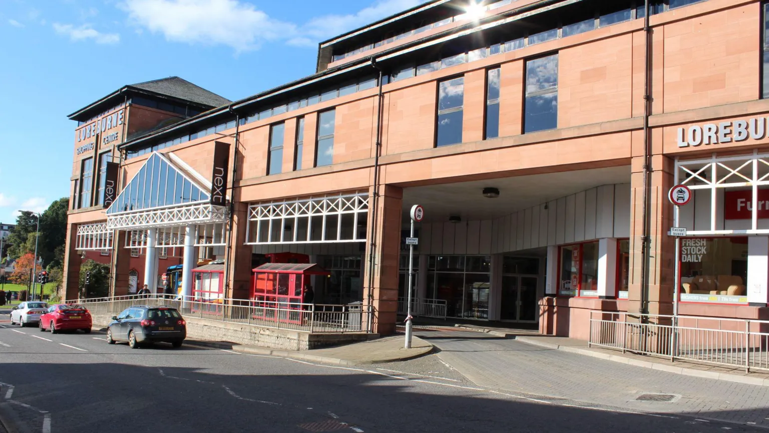Billy McCrorie/ Geograph A shopping centre. There is a bus stop outside it and several cars driving past.