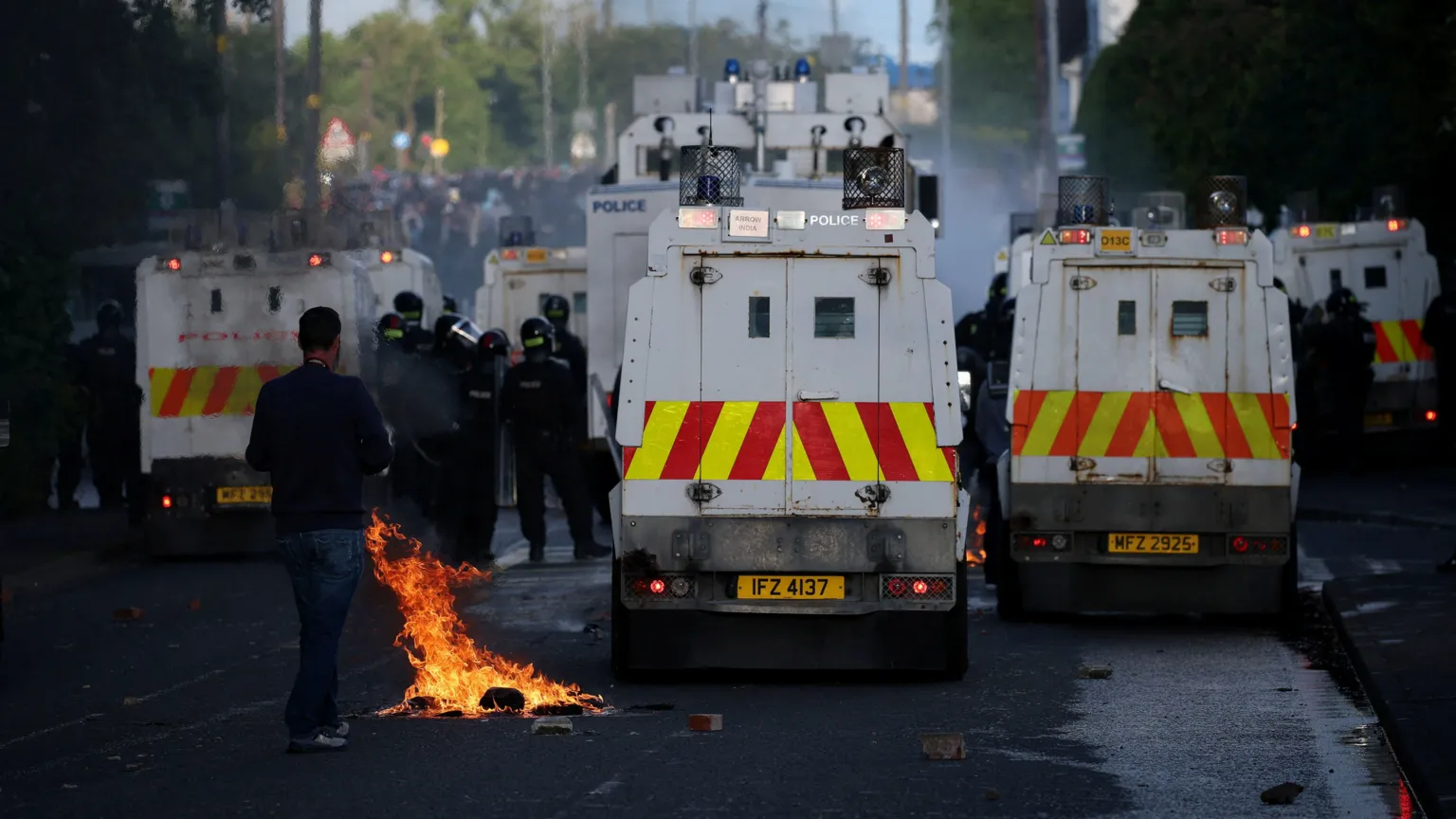  Shows a petrol bomb in flames beside police Land Rovers 