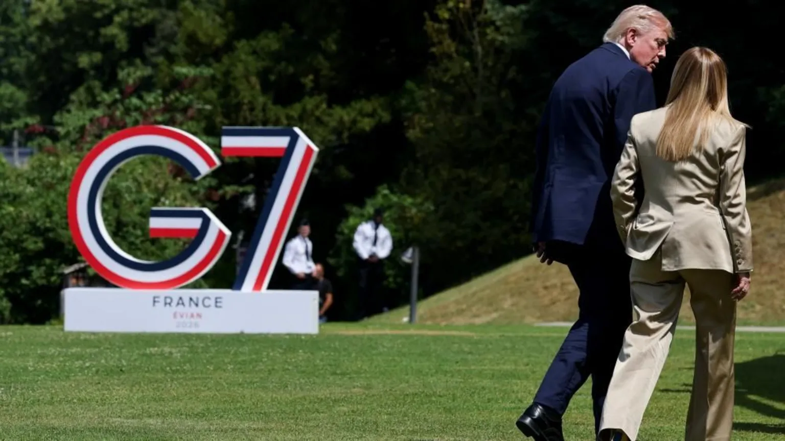Donald Trump and Giorgia Meloni, both wearing suits, walk away from the camera with the G7 logo to their left.