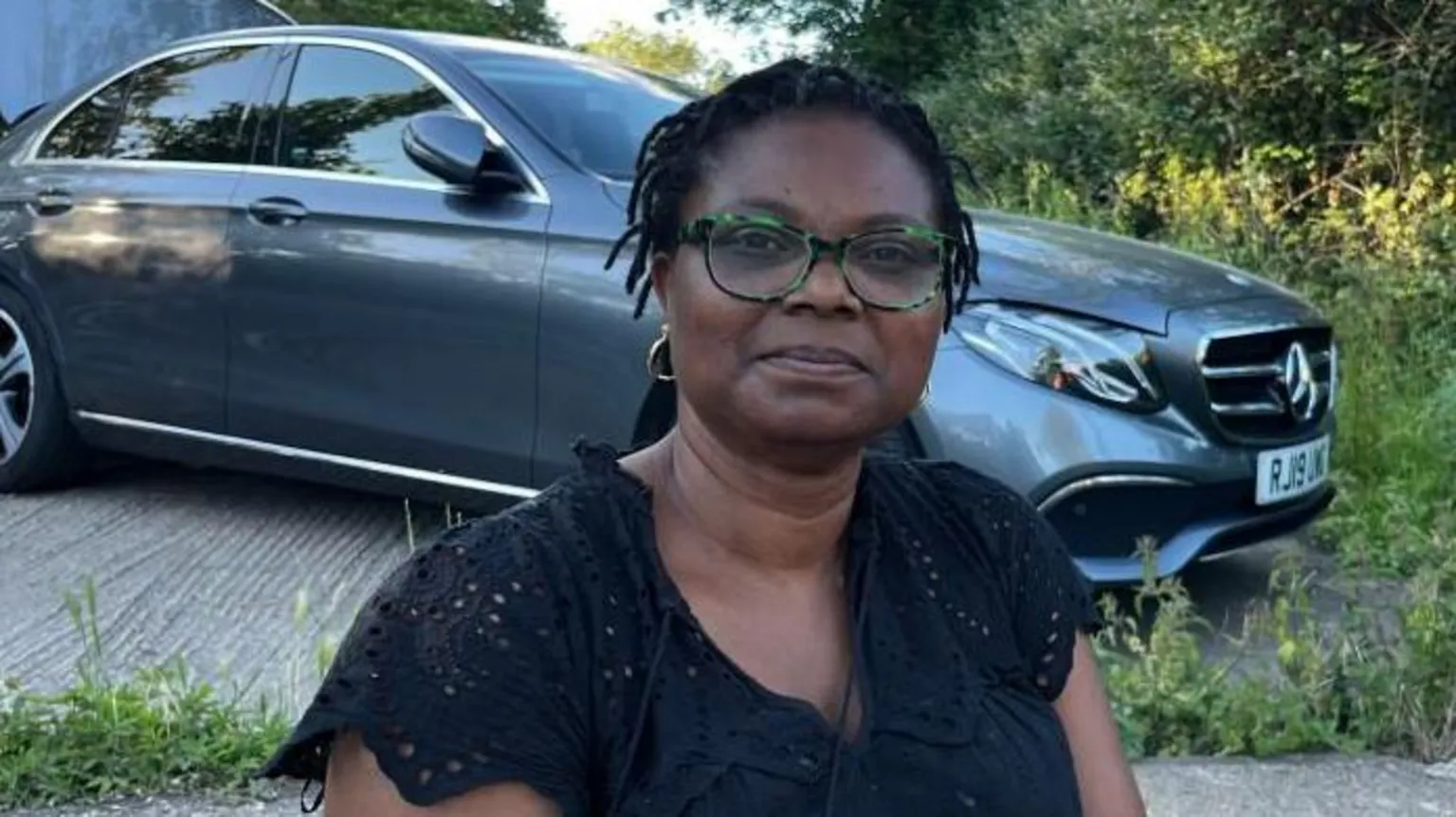 Holly Nichols/BBC Shola Mene, smiling, wearing glasses and a black top