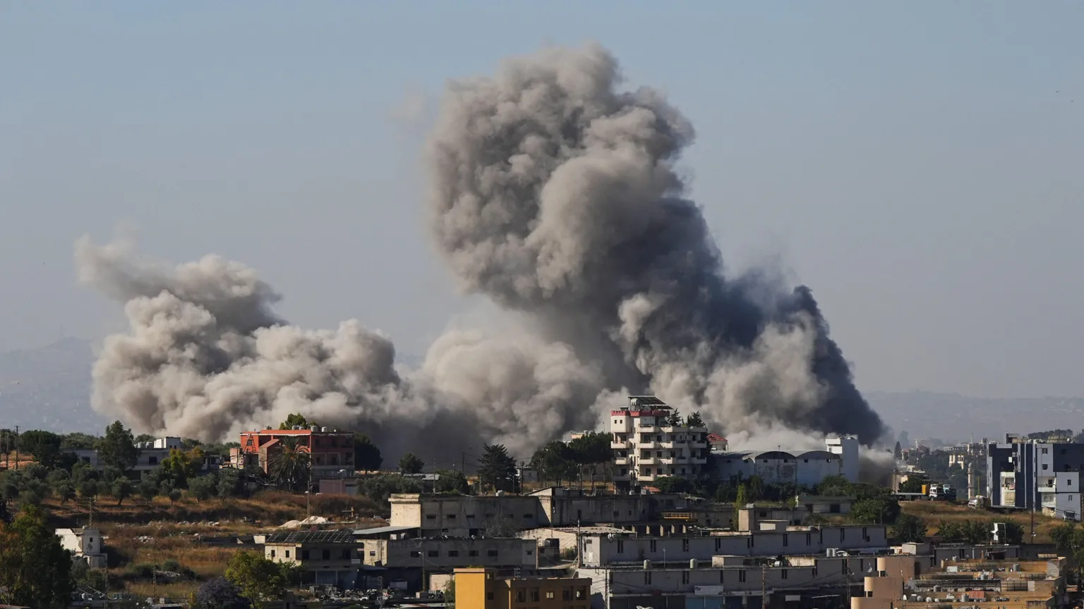 Long shot of a large grey cloud of smoke billowing over a town with some five-storey buildings in southern Lebanon after an Israeli strike.